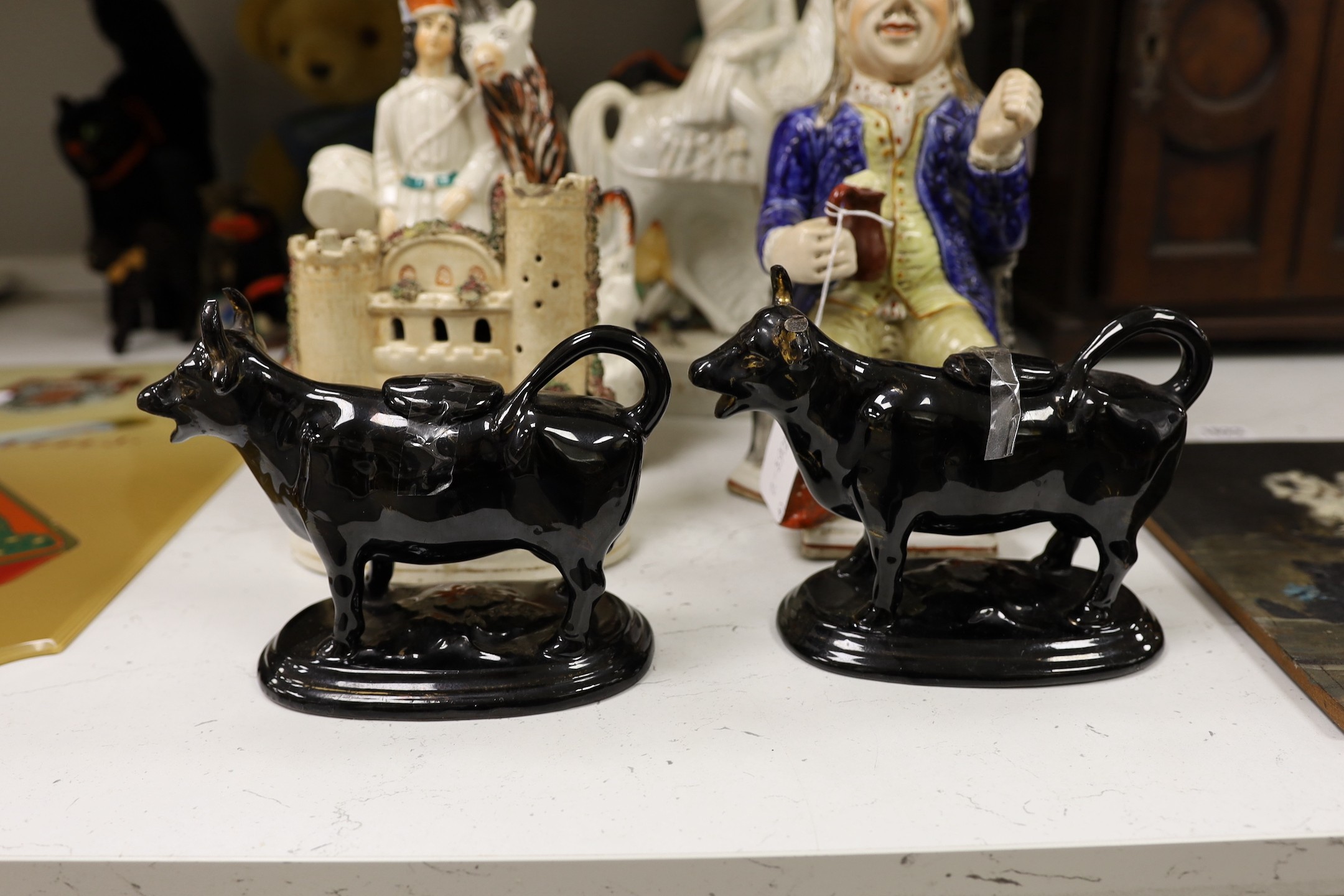 Five Staffordshire pottery figures or groups, tallest 36 cm high two similar Toby jugs, a pair of black glazed cow creamers and a model of a castle